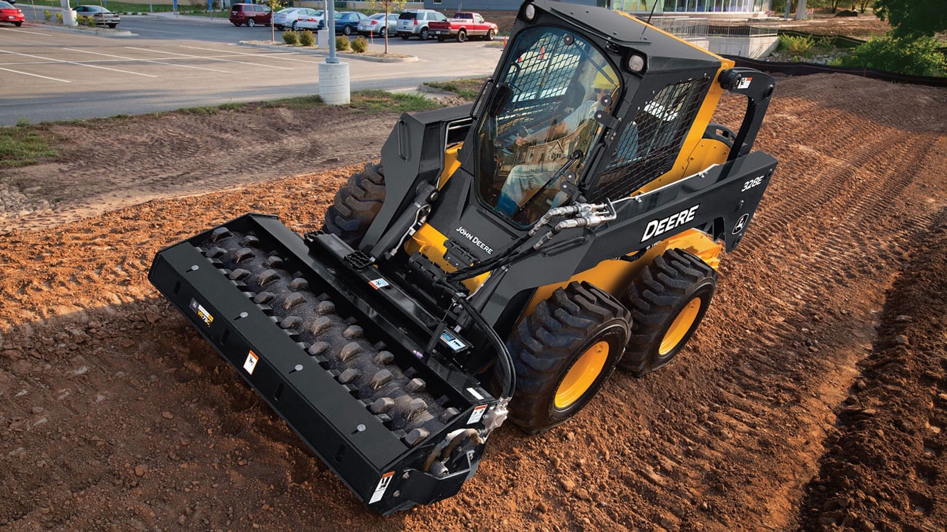 John Deere skid steer with vibratory roller packing dirt on a jobsite.